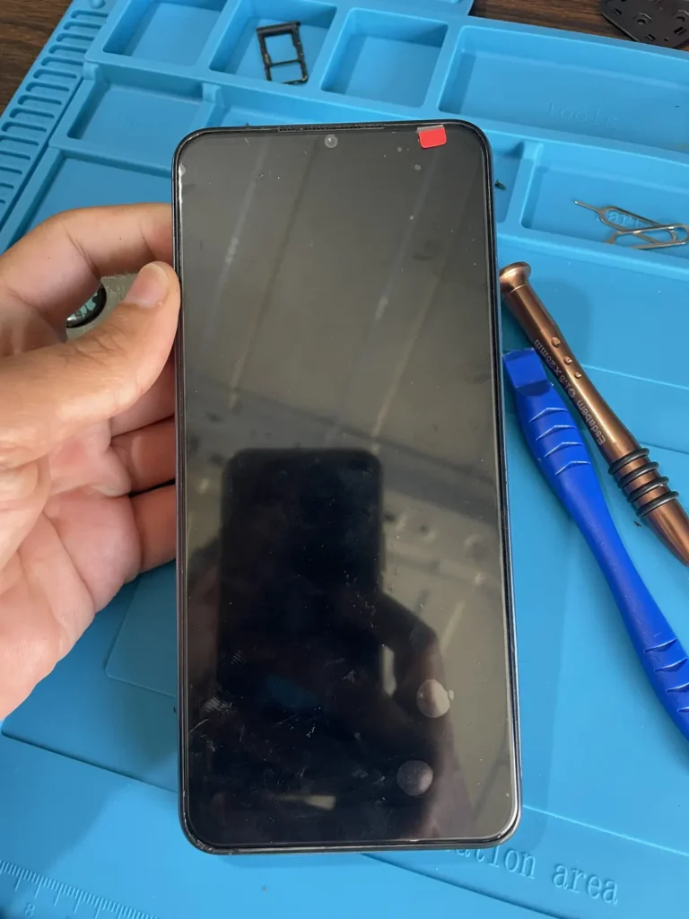 Technician holding a phone with a repair pick to open the frame